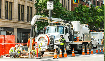 A gallon water truck connected to a sewer and men working