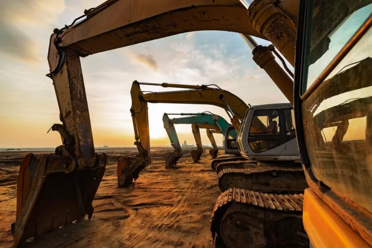A group of excavators on a dirt field at sunset.