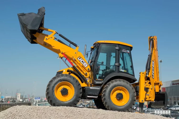 A yellow and black backhoe parked on a gravel lot.