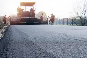 Workers paving a new asphalt road with a road construction machine
